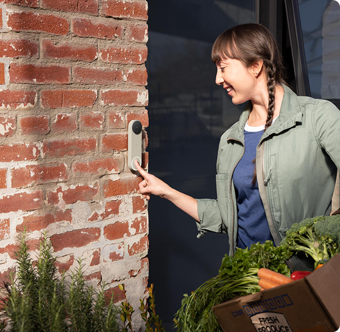 Woman pressing a Google Nest Doorbell while carrying groceries